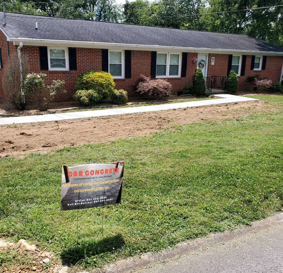 A brick house with black shutters, a concrete walkway, and a