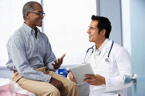 Man in striped shirt consults with a doctor wearing a white coat in a medical setting. Both are smiling.