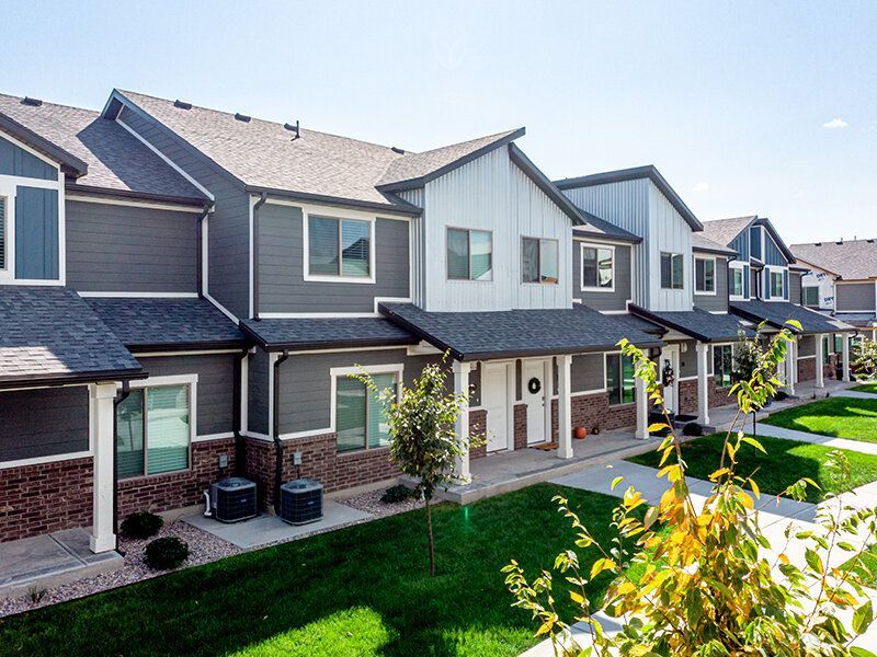 Row of modern townhouses with gray and white exteriors, green lawns, and a sunny day.