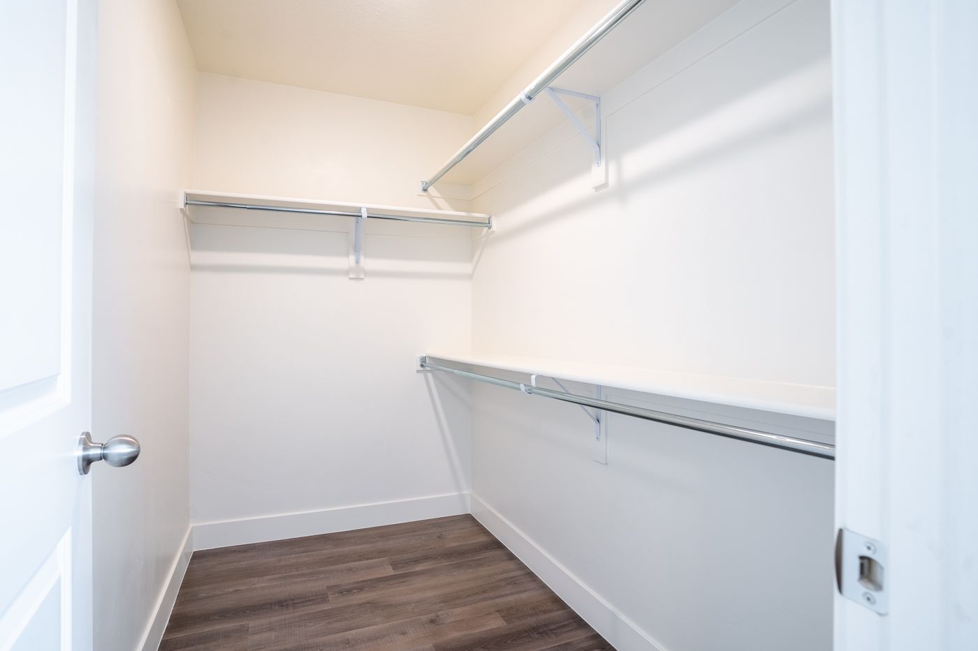 Walk-in closet with white walls, dual hanging rods, and a wood-look floor.