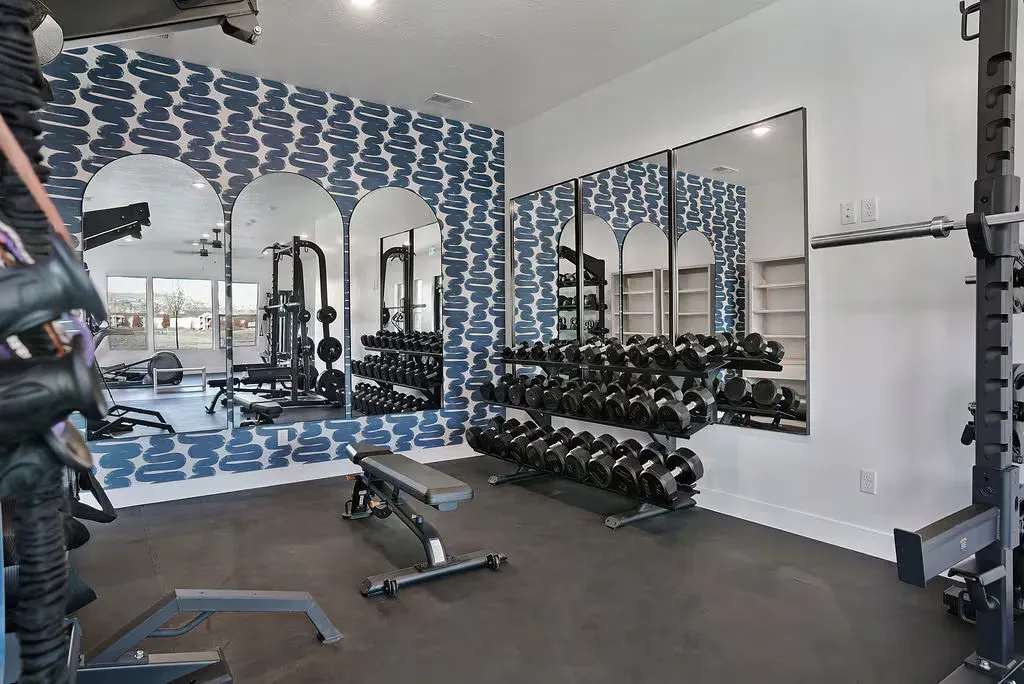Home gym with weights, mirrors, and bench, featuring patterned blue wallpaper and rubber flooring.