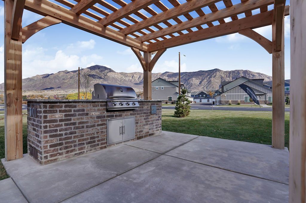 Outdoor brick BBQ grill under a wooden pergola in a communal courtyard with distant mountains.