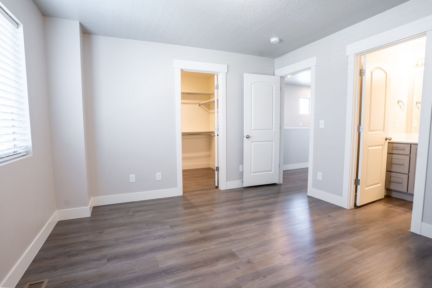 Empty bedroom with gray walls, a window with blinds, and an open closet.