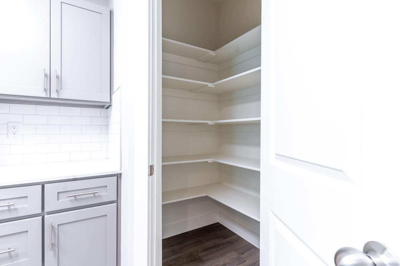Open white pantry with multiple shelves beside white kitchen cabinets.