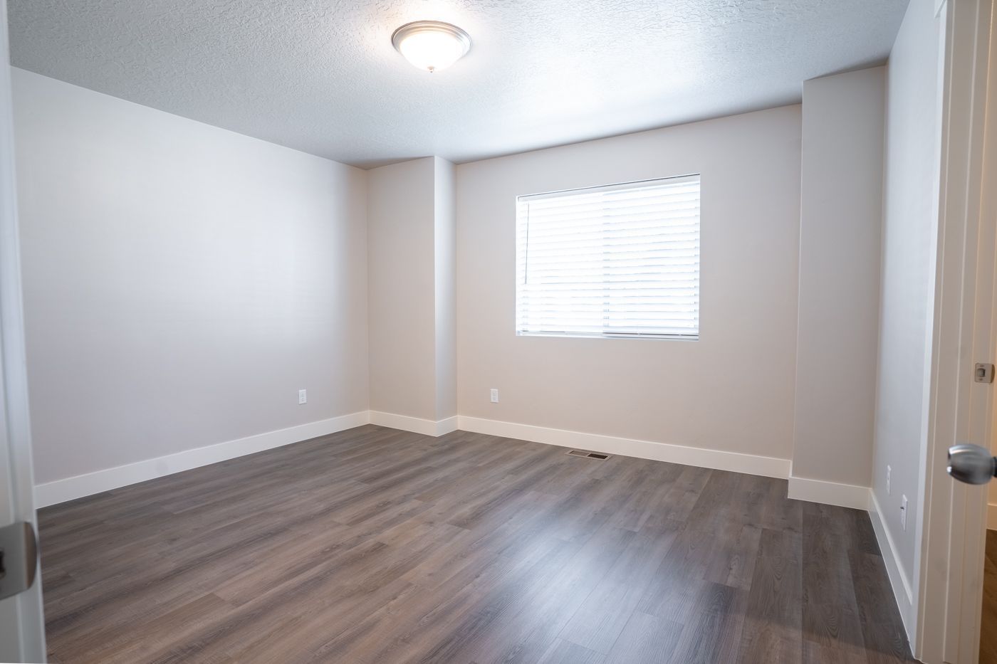 Empty apartment living room with gray walls, window with blinds, and wood-like flooring.