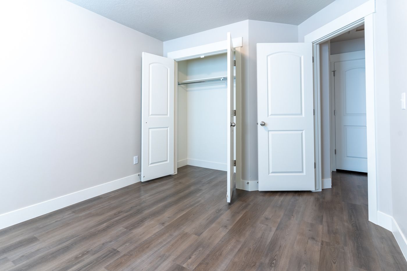 Empty bedroom with open double-door closet and wood flooring.