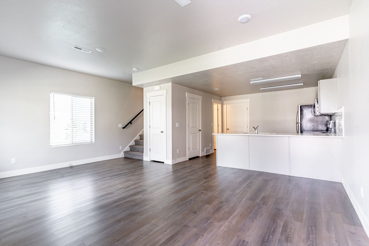 Open-plan living area with gray laminate flooring, white walls, and a kitchen with a long island.