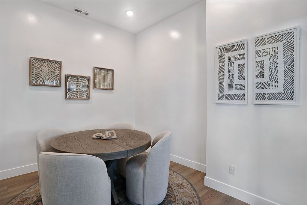 Small dining nook with a round wooden table and four light-gray upholstered chairs against white walls.