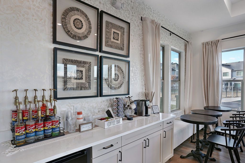 Resident lounge with a coffee bar, white cabinetry, framed wall art, and window seating.