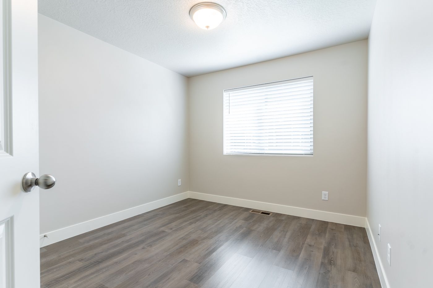 Empty interior bedroom with gray flooring, light gray walls, and a window with blinds.