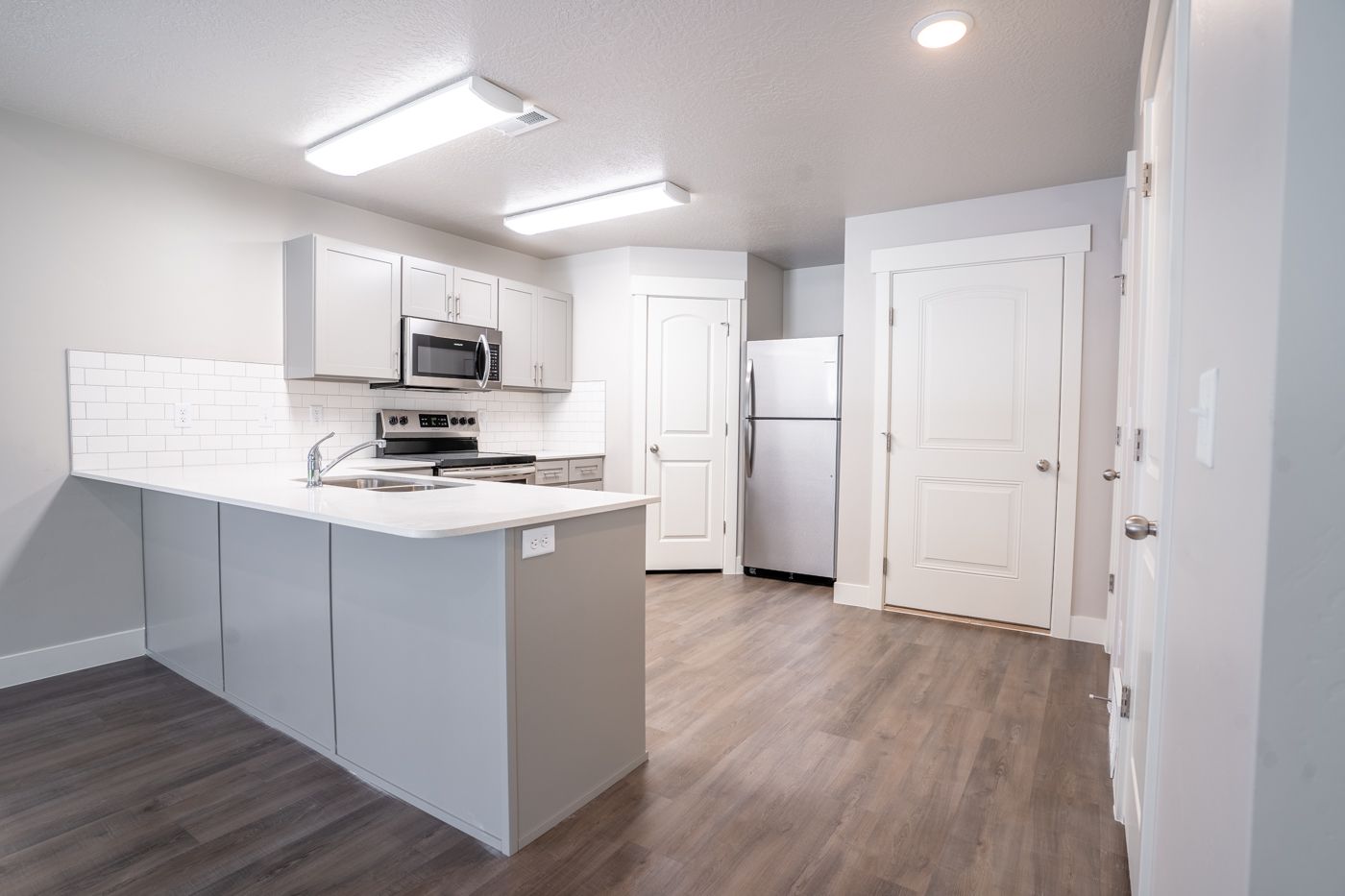 Modern kitchen with white cabinets, stainless steel appliances, island, and white tile backsplash.