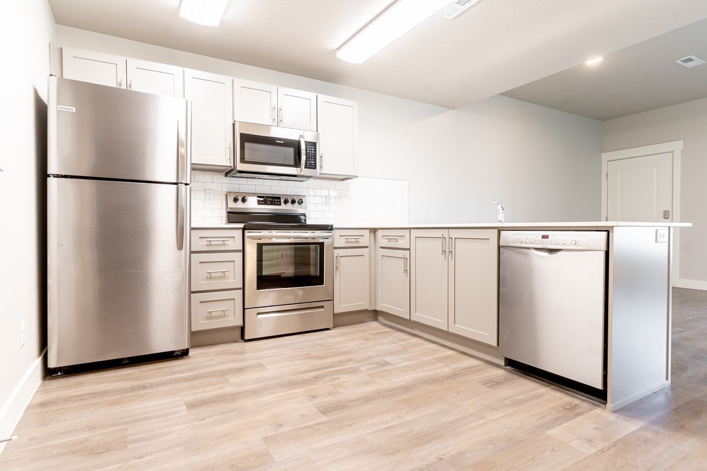 Modern apartment kitchen with stainless steel fridge, range, microwave, and dishwasher.