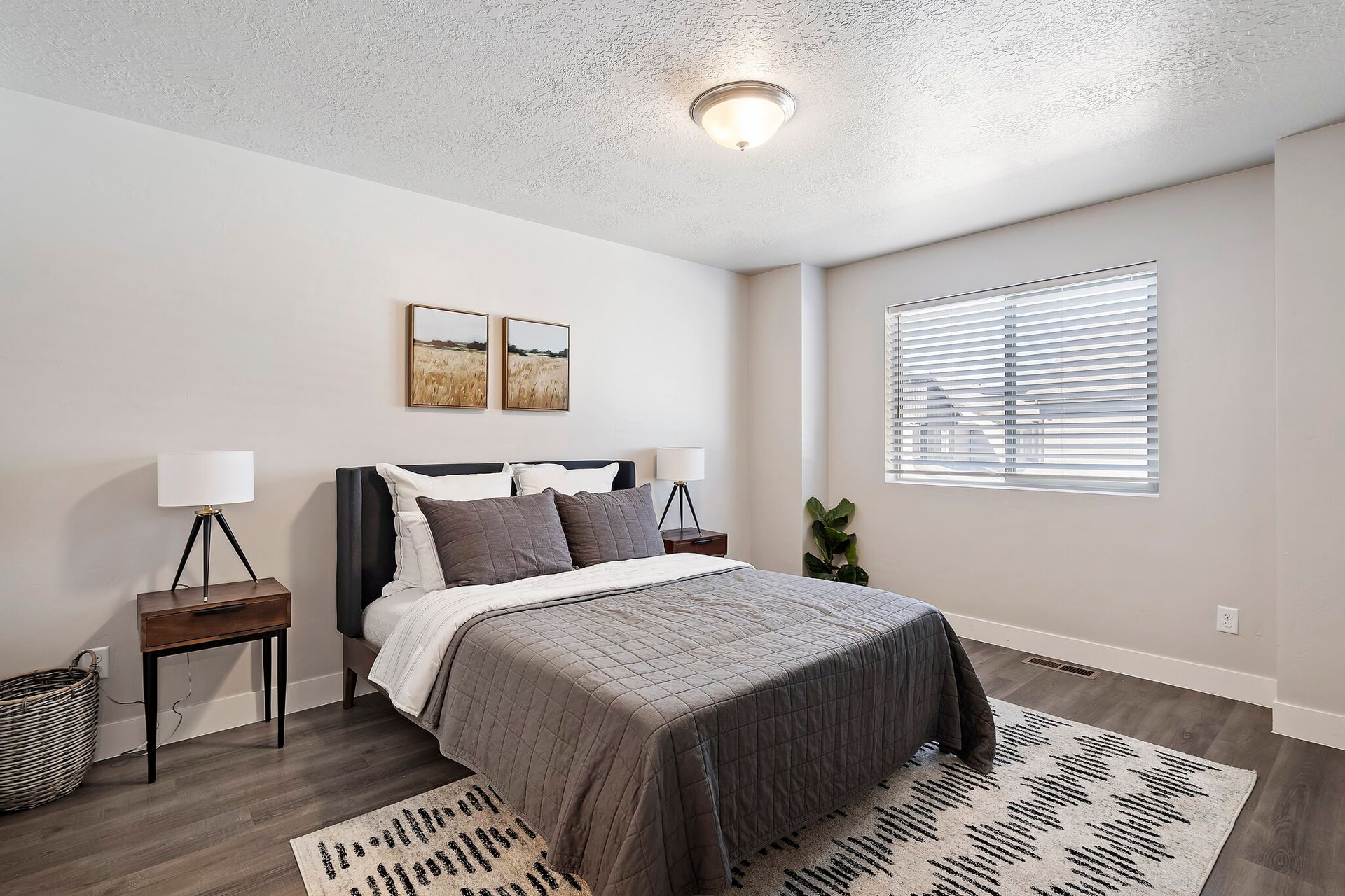Bedroom in a modern apartment with a bed, two nightstands, lamps, and a window with blinds.