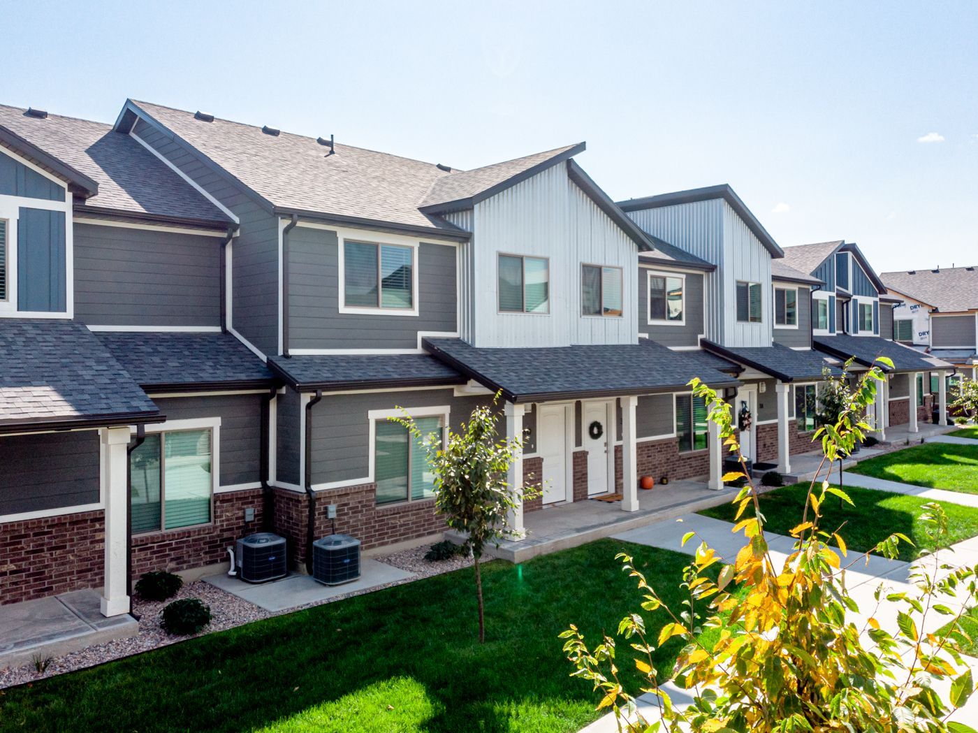 Row of townhouse-style apartment buildings with gray siding, brick bases, and green lawn.