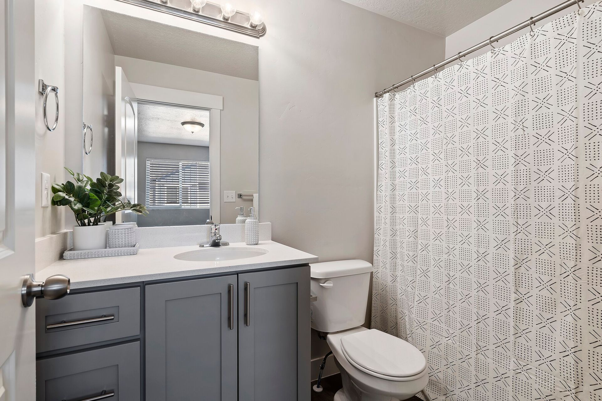 Bathroom with gray vanity, white countertop, large mirror, toilet, and patterned shower curtain.