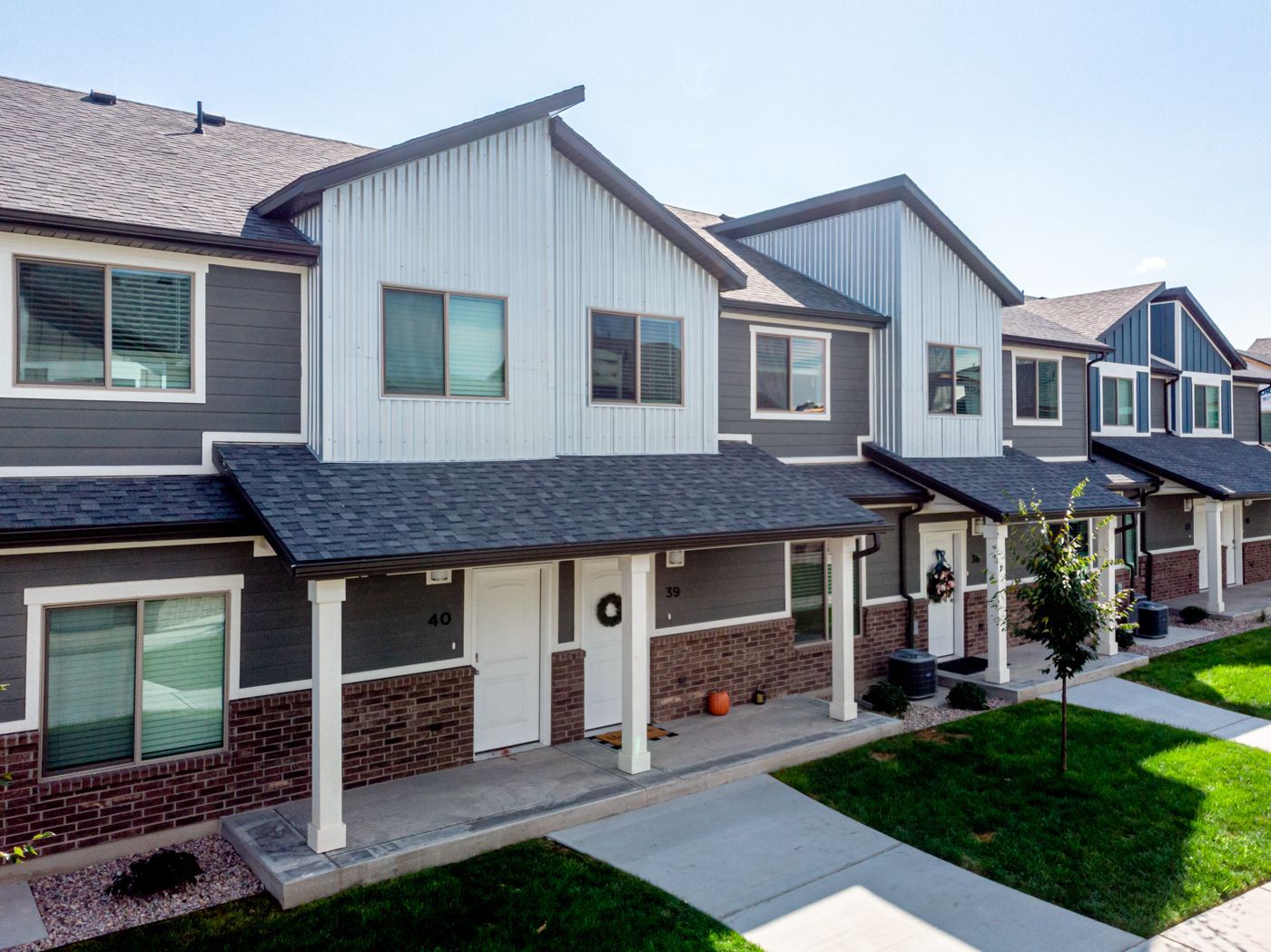 Row of townhouse-style apartments with gray siding and brick bases along a front walkway.