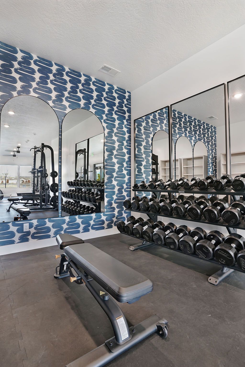 Indoor gym with a bench, row of dumbbells, and mirrored wall.