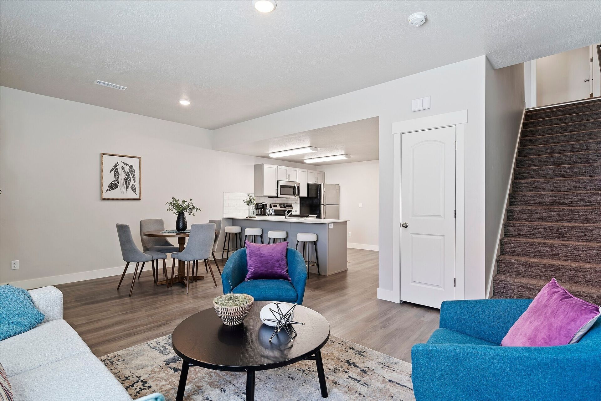 Open-concept living area with a sofa, blue chairs, round coffee table, and kitchen island.