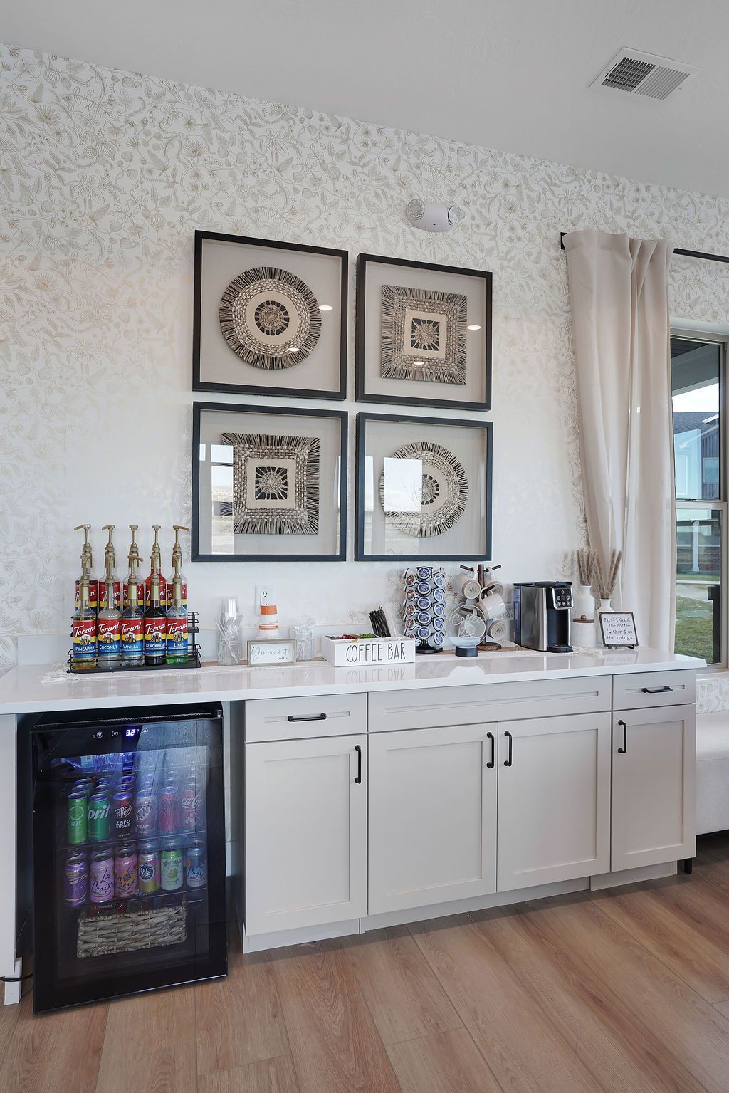 Coffee bar in a modern apartment community lounge with beverages, cups, and a small fridge.