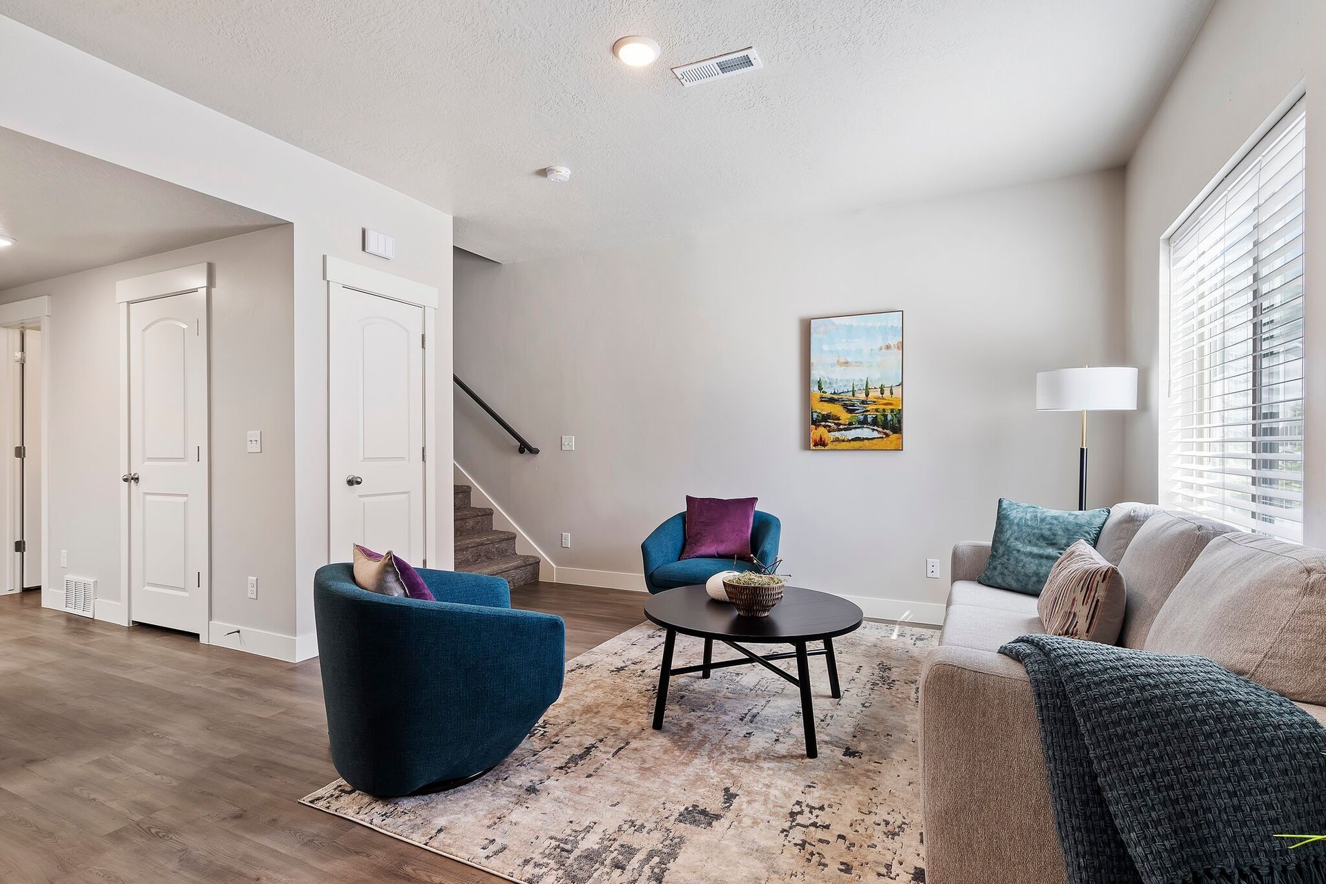 Bright living room in an apartment with a beige sofa, two blue chairs, and a round coffee table.