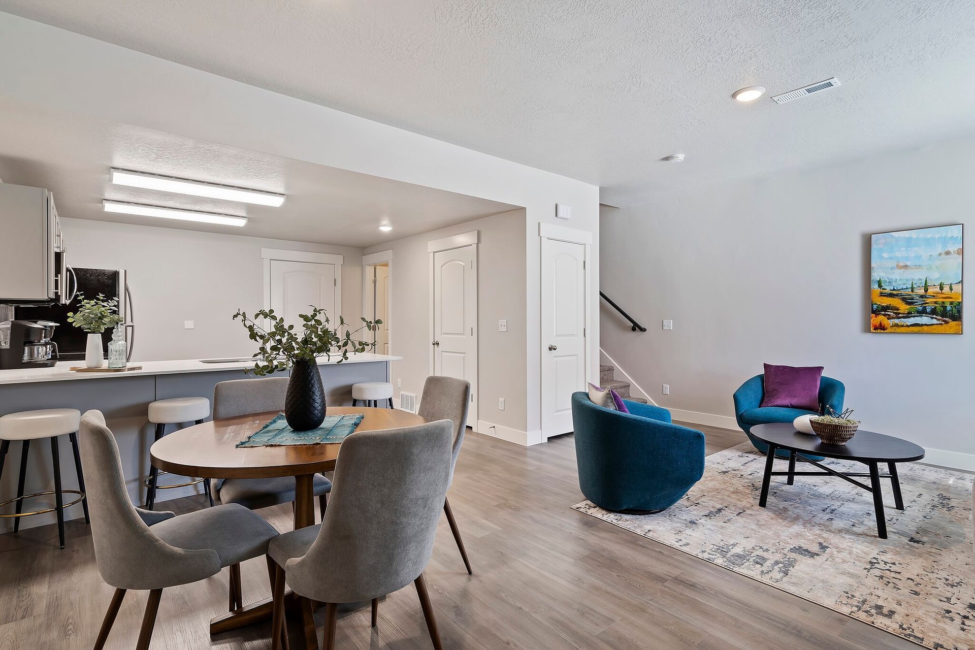 Open-concept living area with a kitchen island, dining table, and blue lounge chairs.