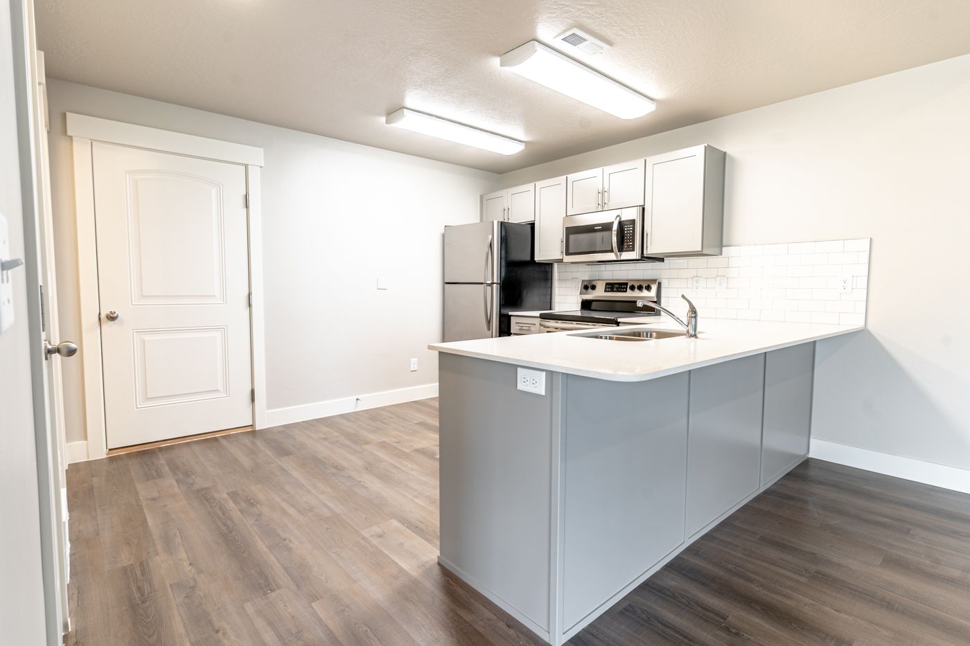 Bright kitchen with an island, stainless steel fridge, oven, microwave, and white tile backsplash.