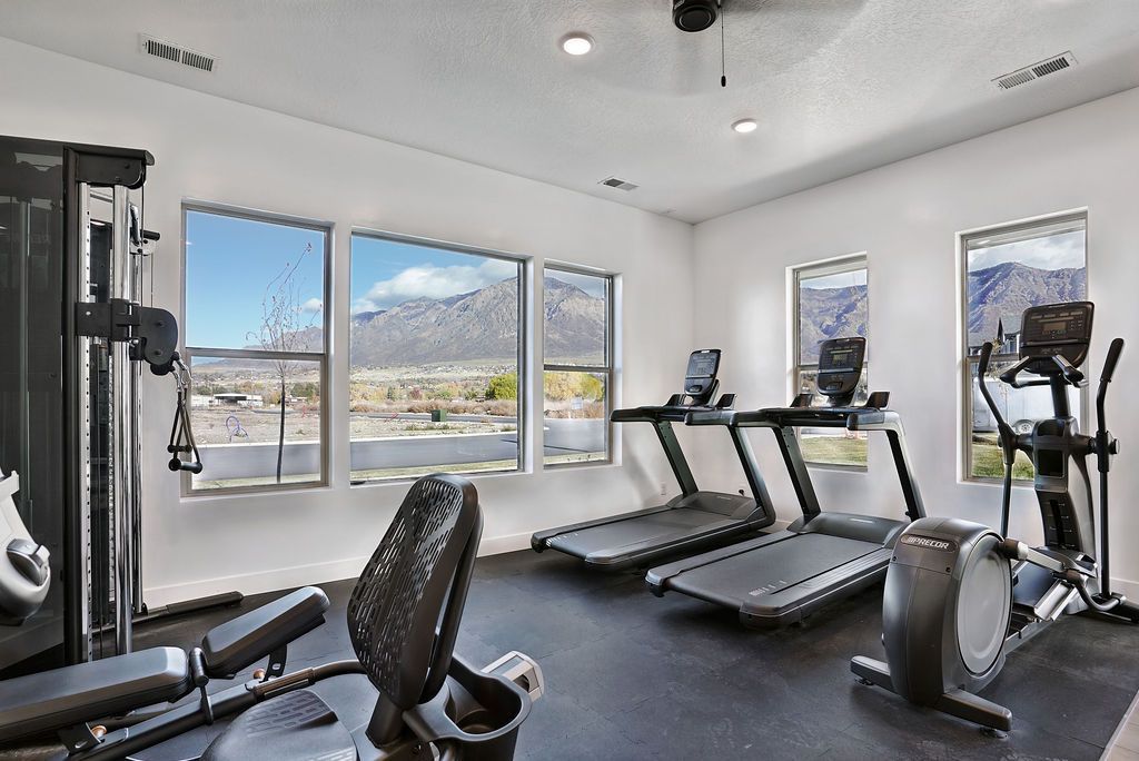 Bright apartment gym with treadmills, elliptical, weight machines, and mountain-view windows.