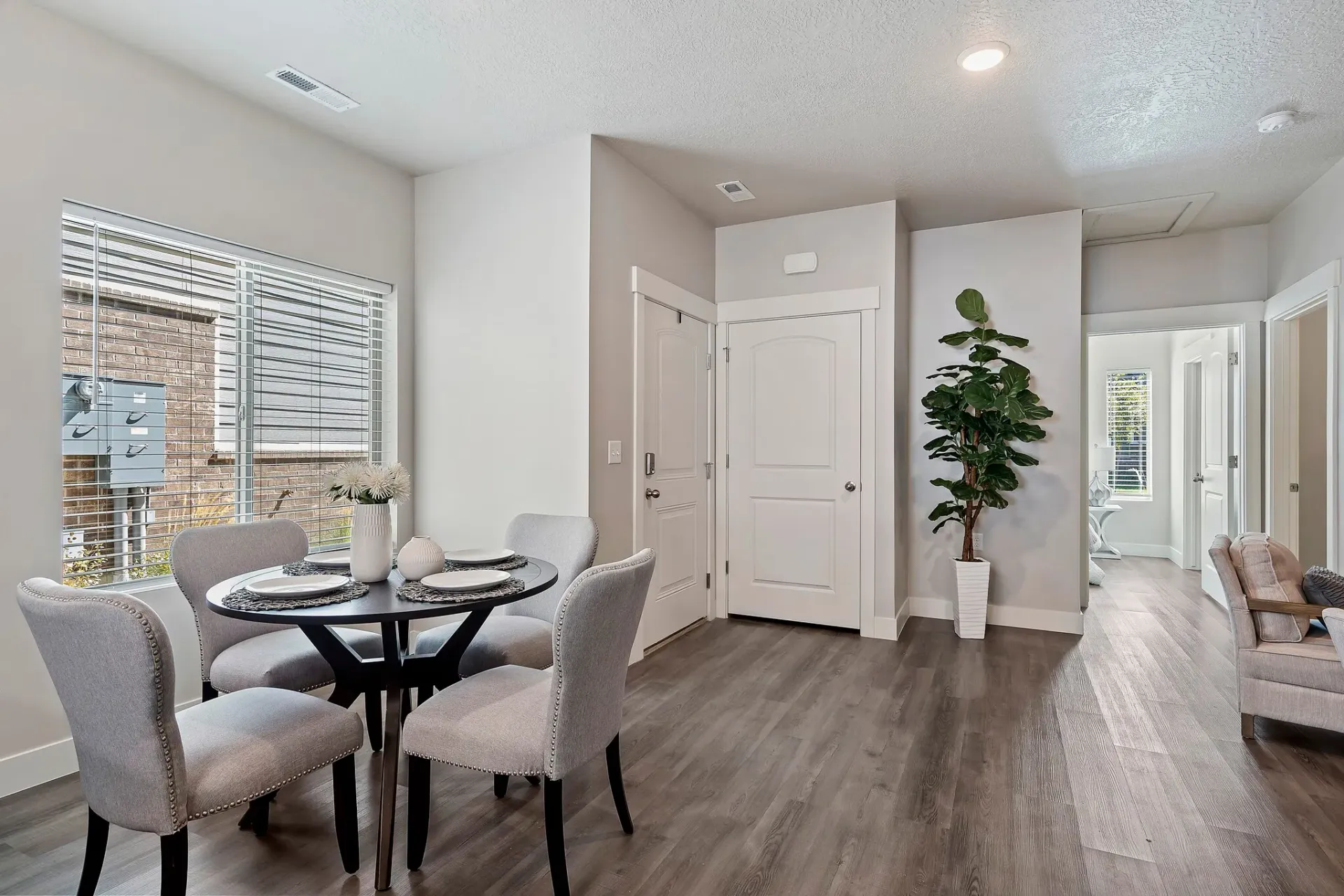 Dining area with a round table and four upholstered chairs by a large window in a modern apartment.