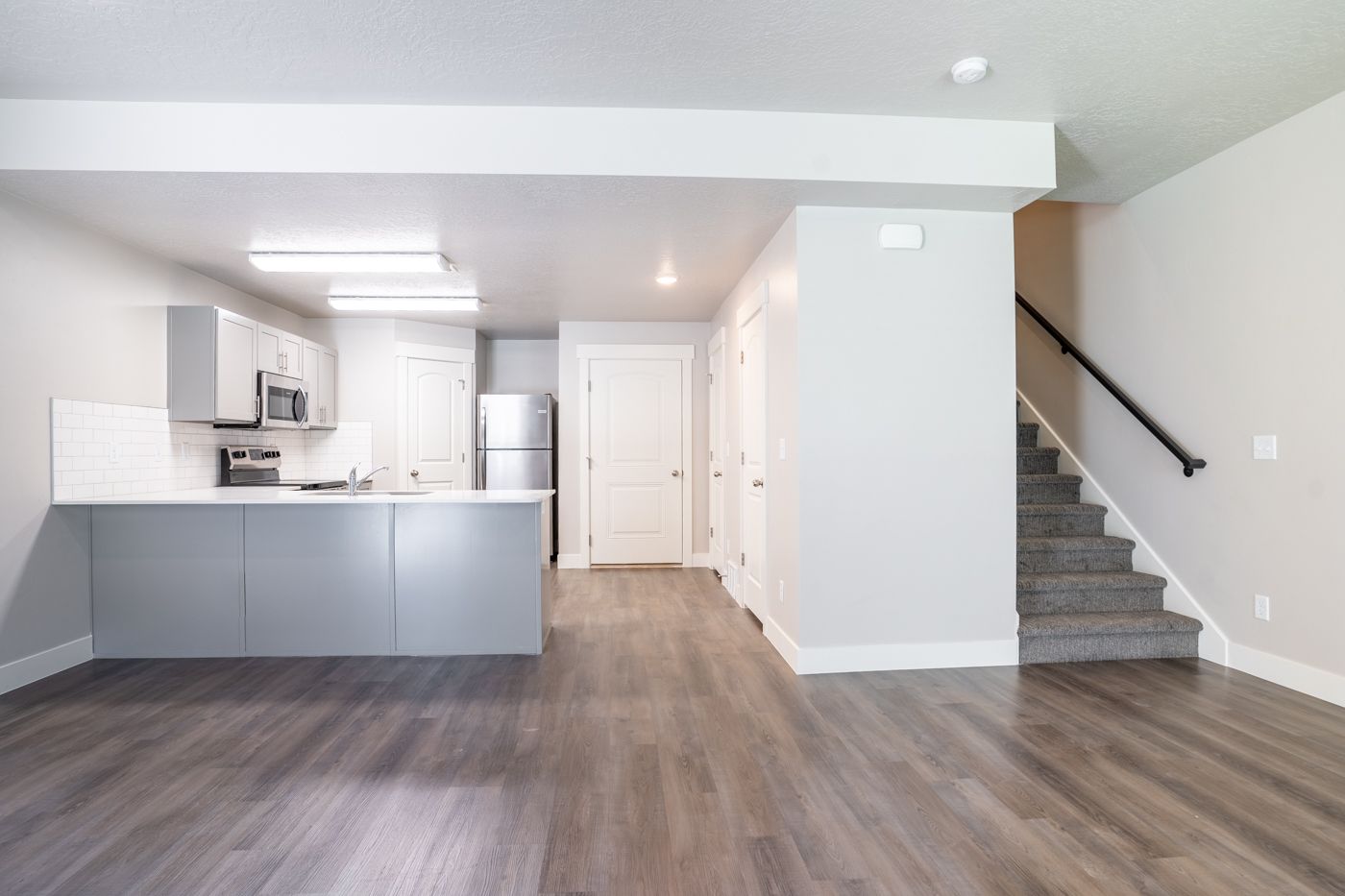 Open-concept kitchen with island, gray cabinets, white backsplash, and stainless steel appliances.