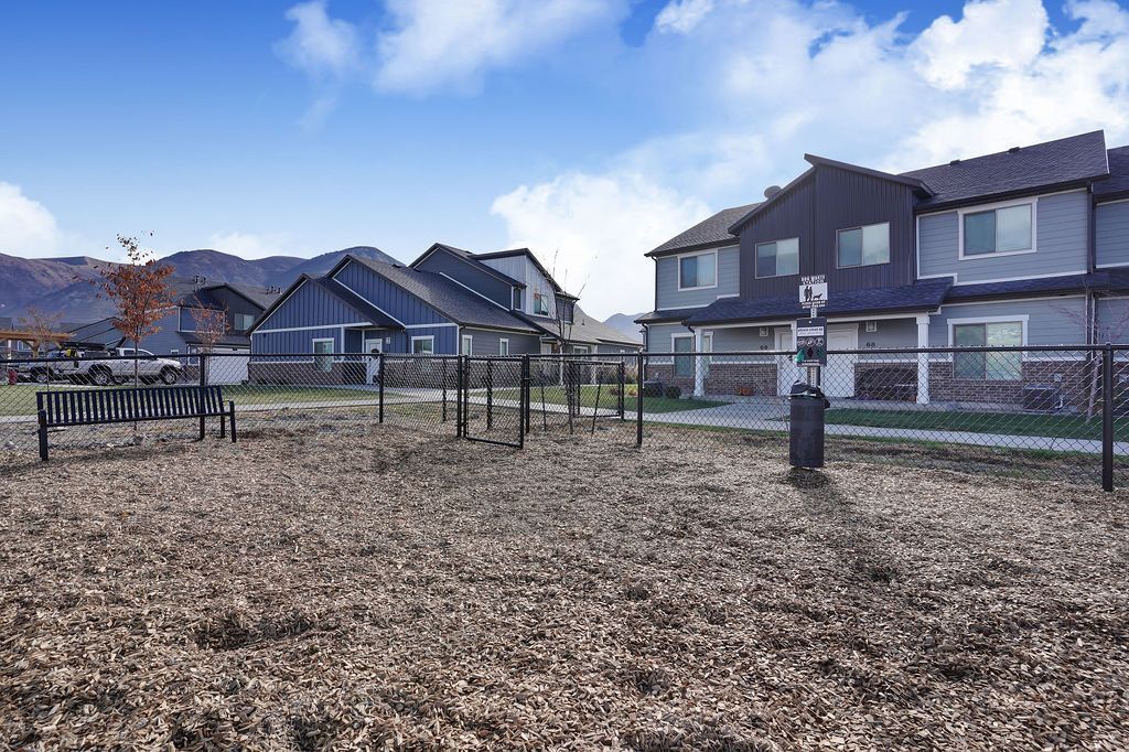 Outdoor community area with a chain-link fence, bench, and apartment buildings in the background.