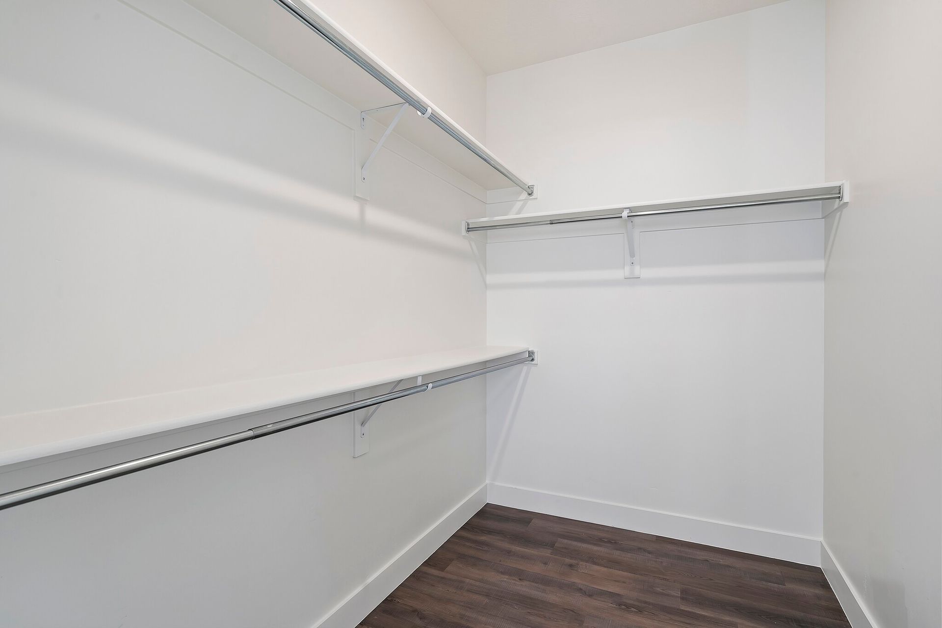 White walk-in closet with multiple hanging rods and shelves along the walls.