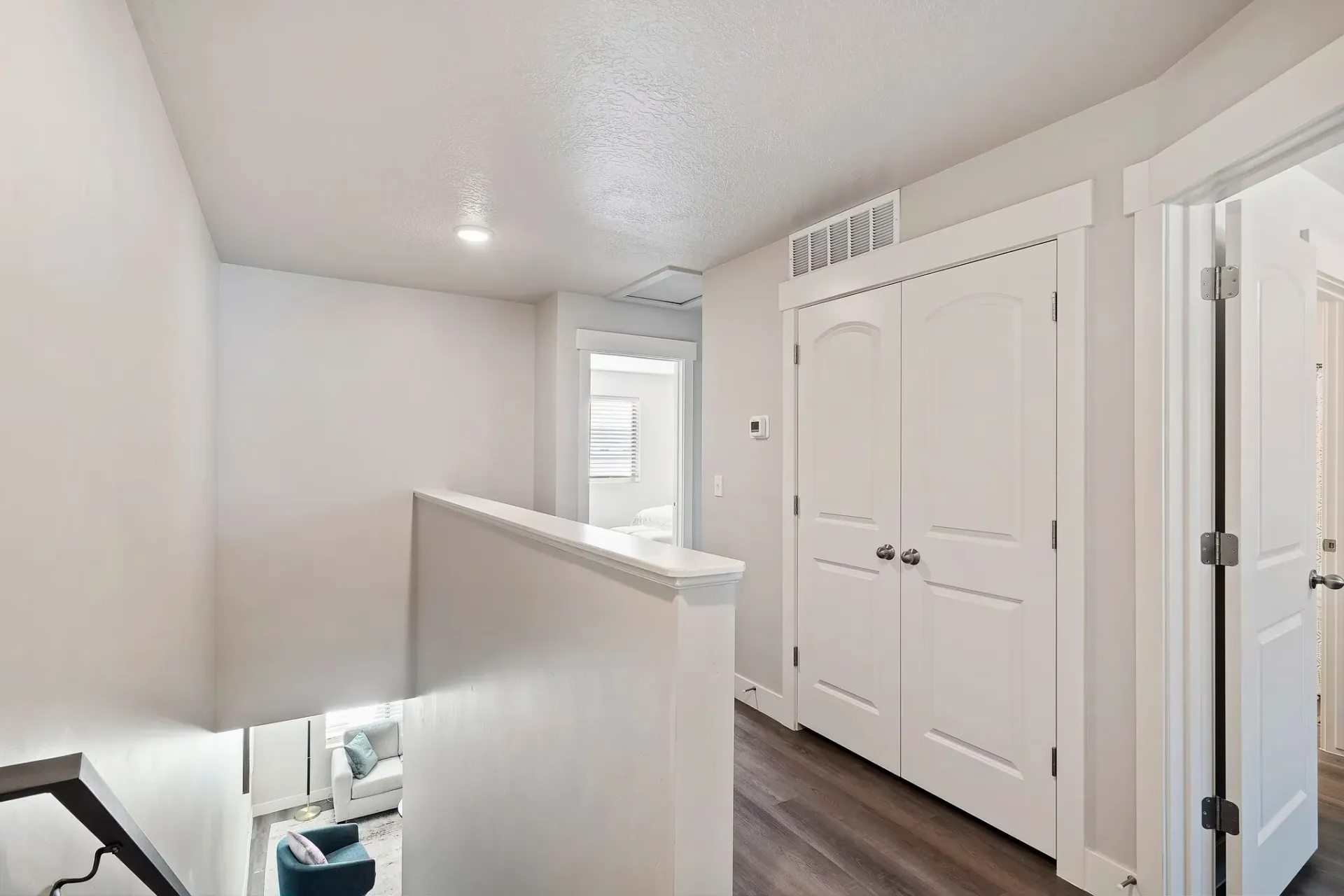 Bright upper-floor hallway with white walls, a short railing, stairs down, and double closet doors.