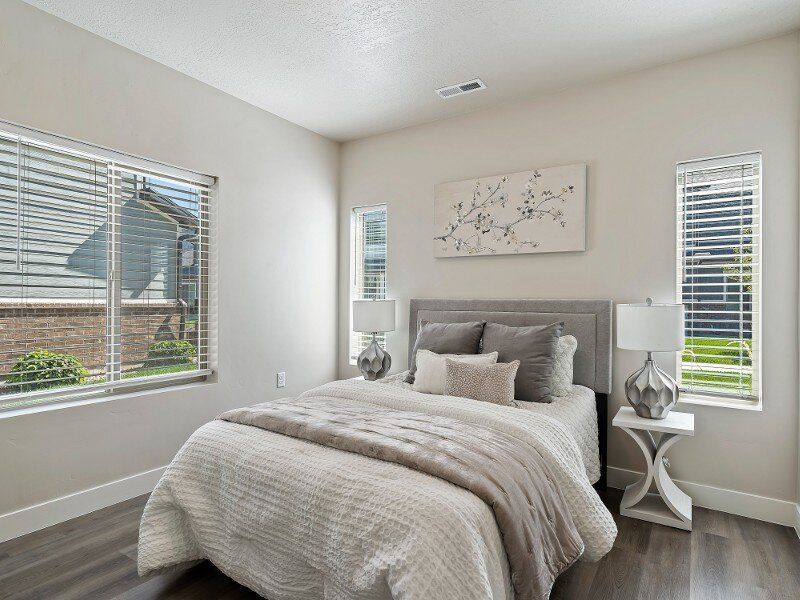 Bedroom with bed, lamps, and windows with blinds. Neutral color palette.