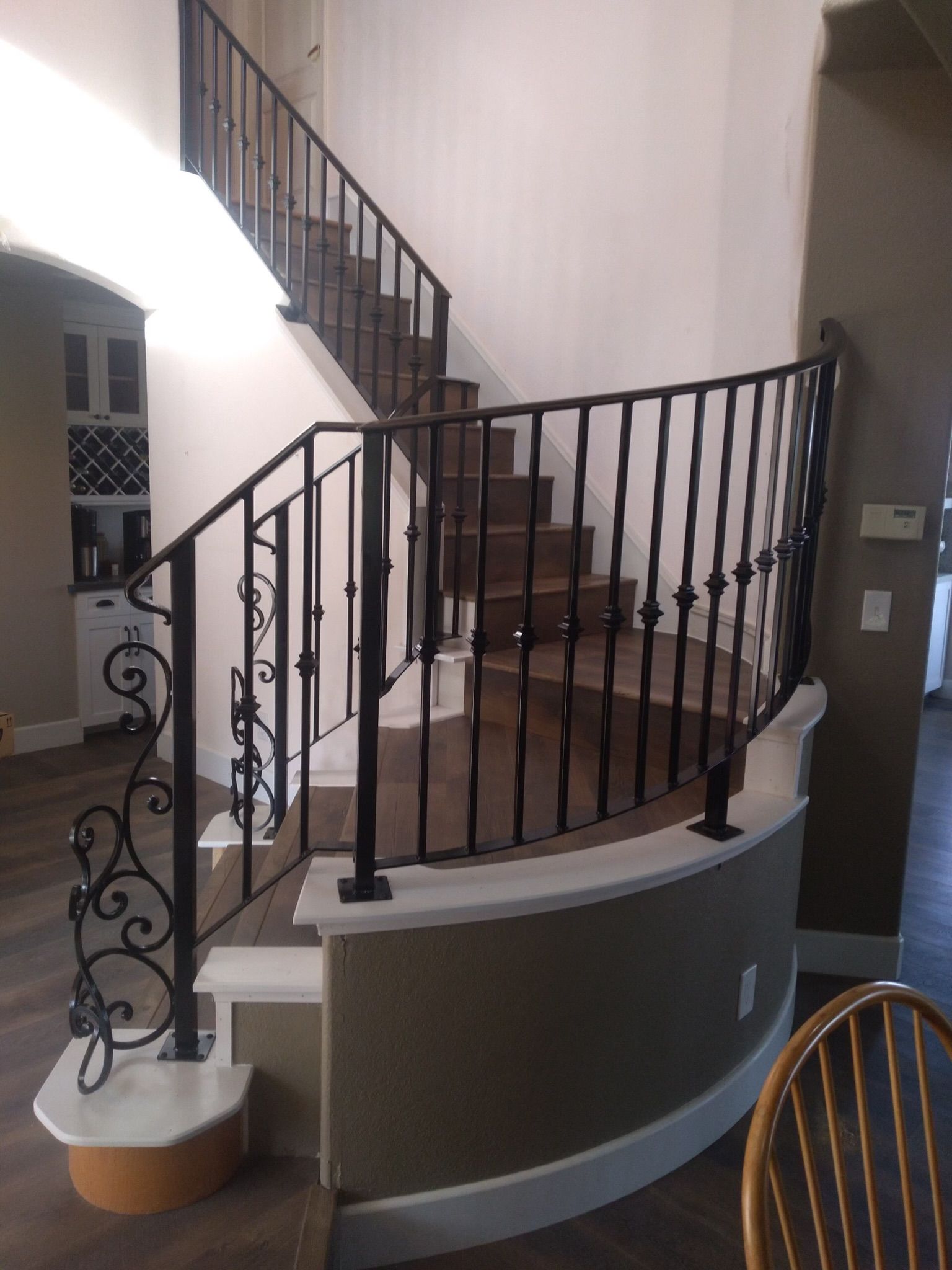 Curved staircase with black iron railing; carpeted steps, white and olive green walls.
