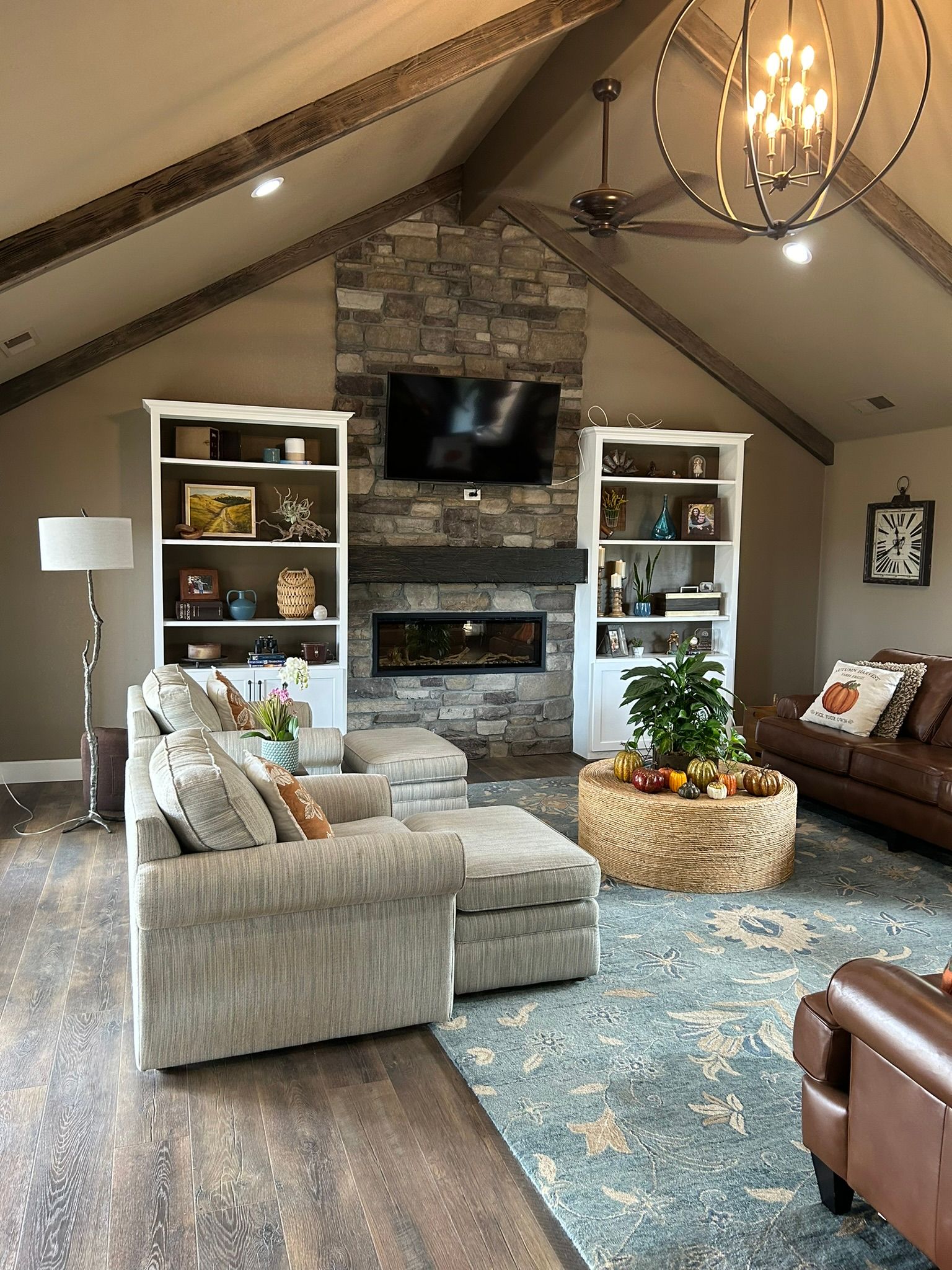 Living room with stone fireplace, TV, built-in shelves, sectional sofa, and a woven basket.