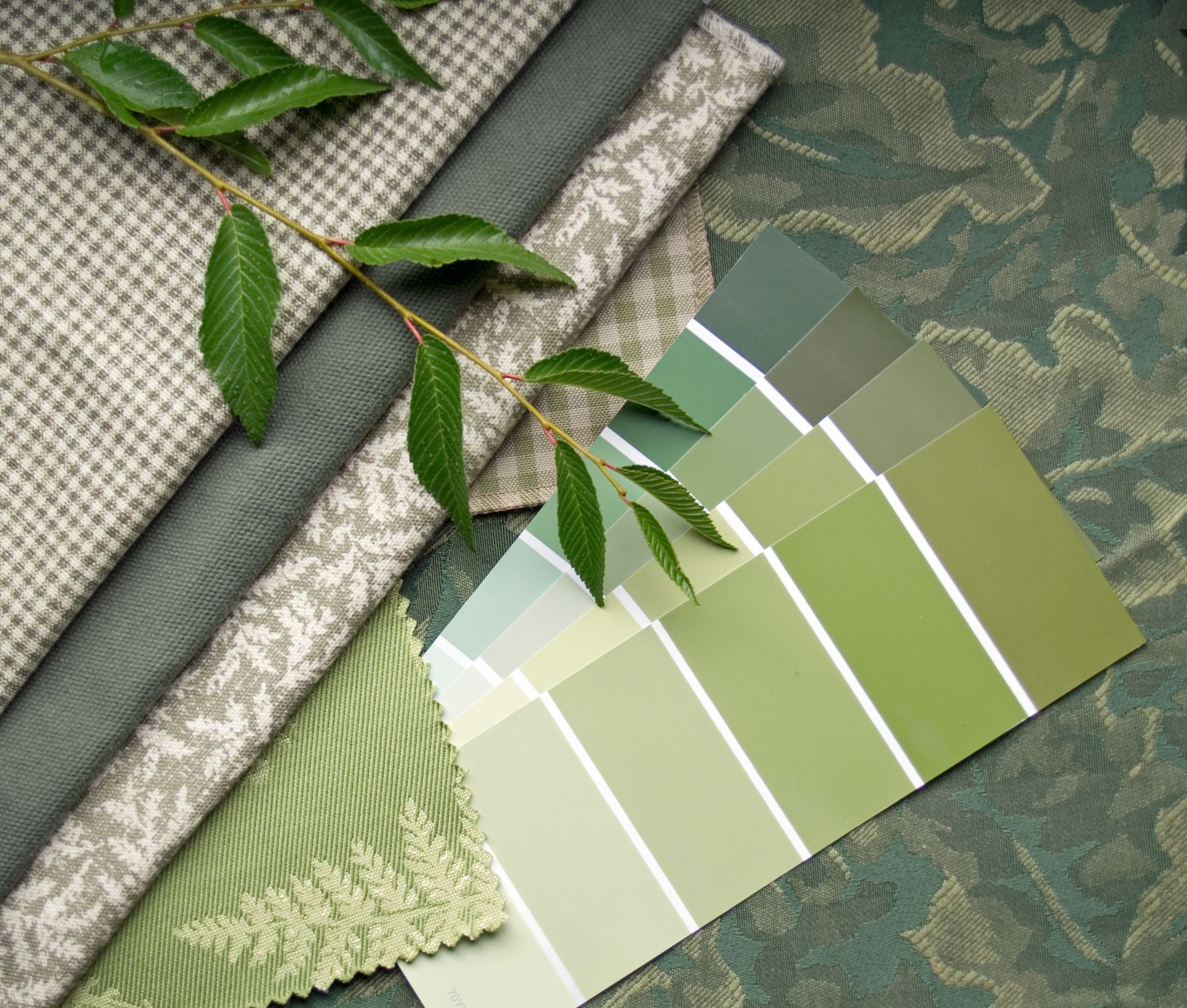 Fabric swatches and paint color swatches in shades of green, with a sprig of green leaves.