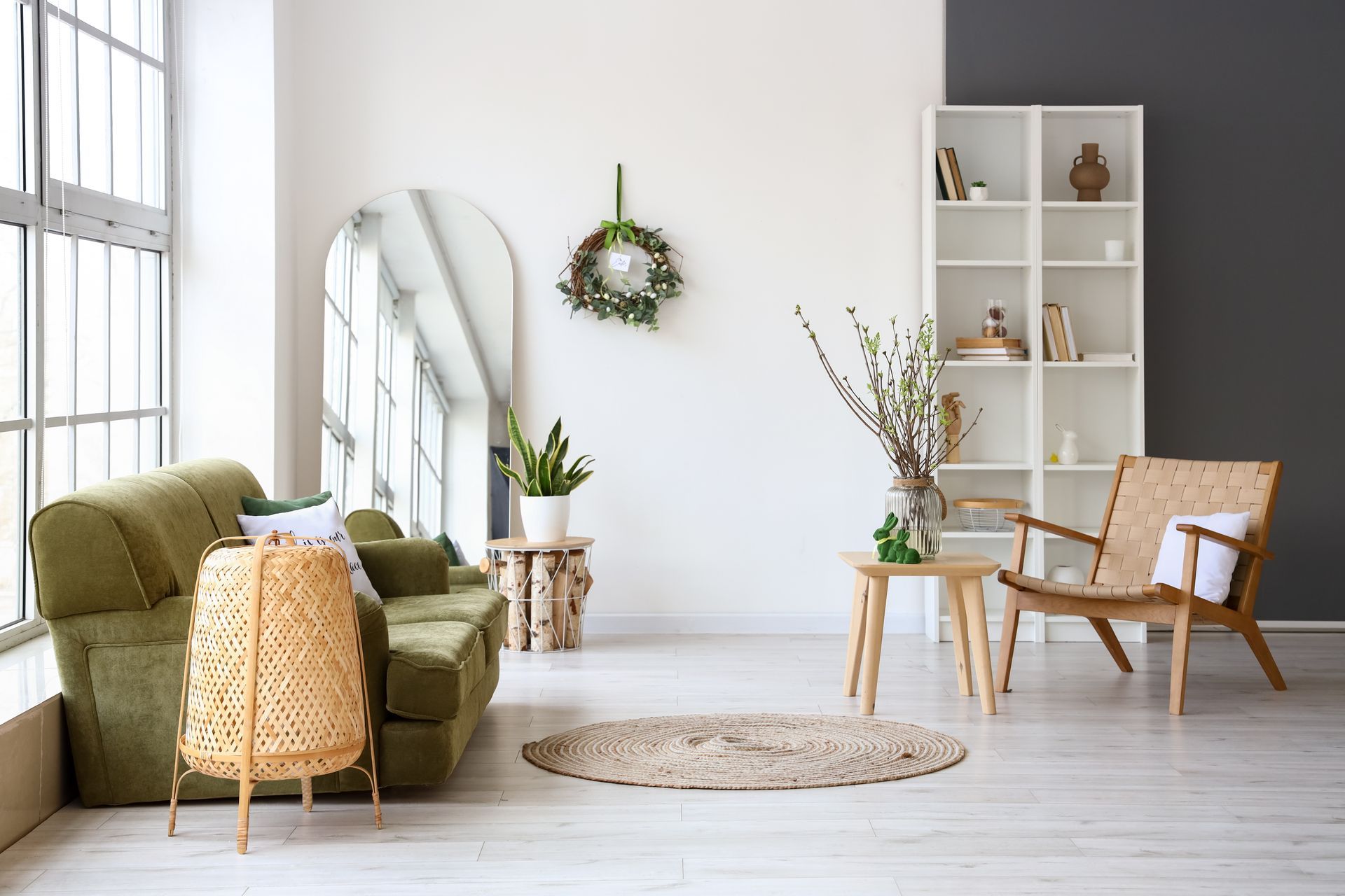 A bright living room with green sofa, wooden chair, bookshelf, and large arched mirror.