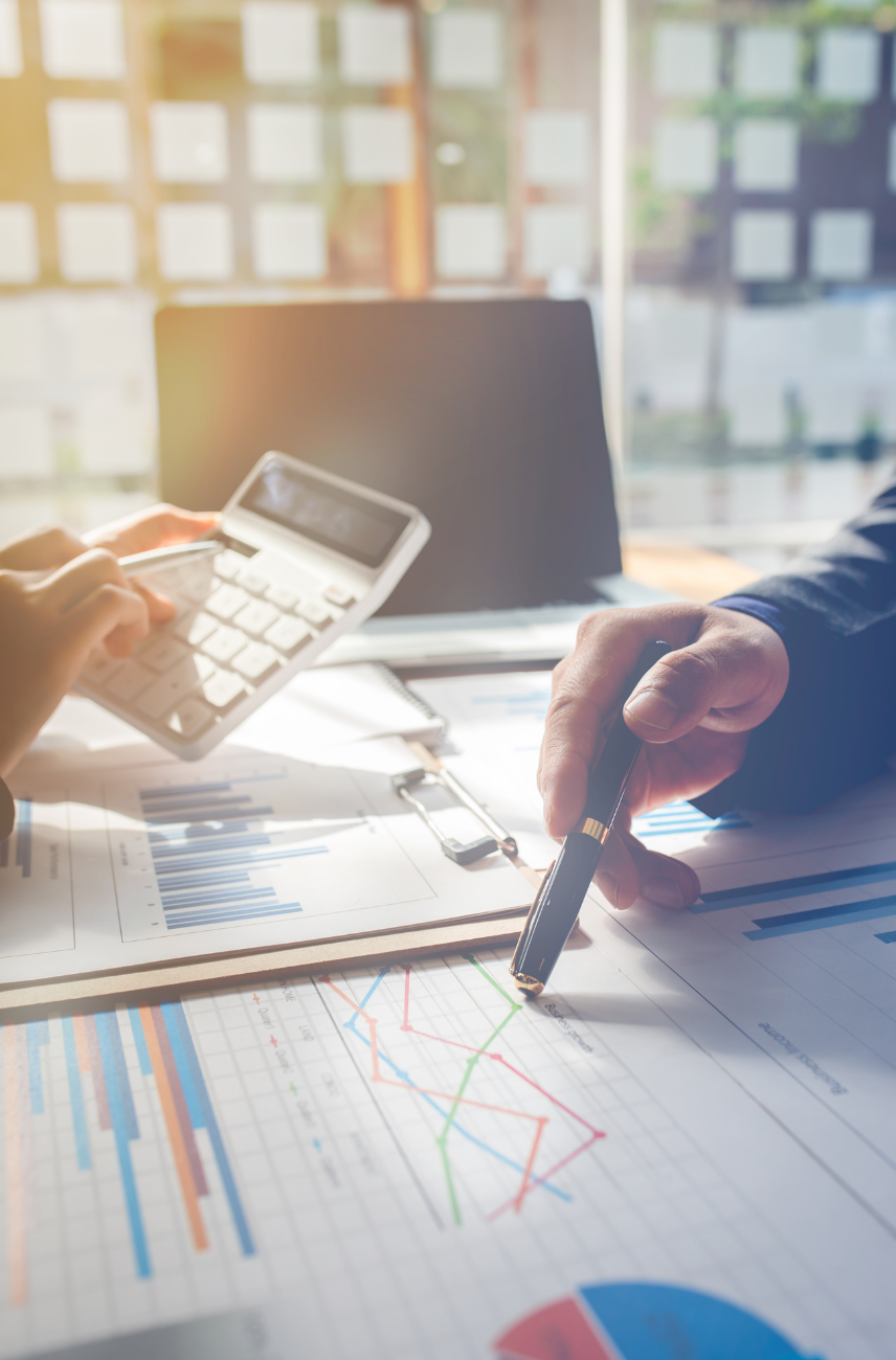 A man is using a calculator while another man is pointing at a graph.