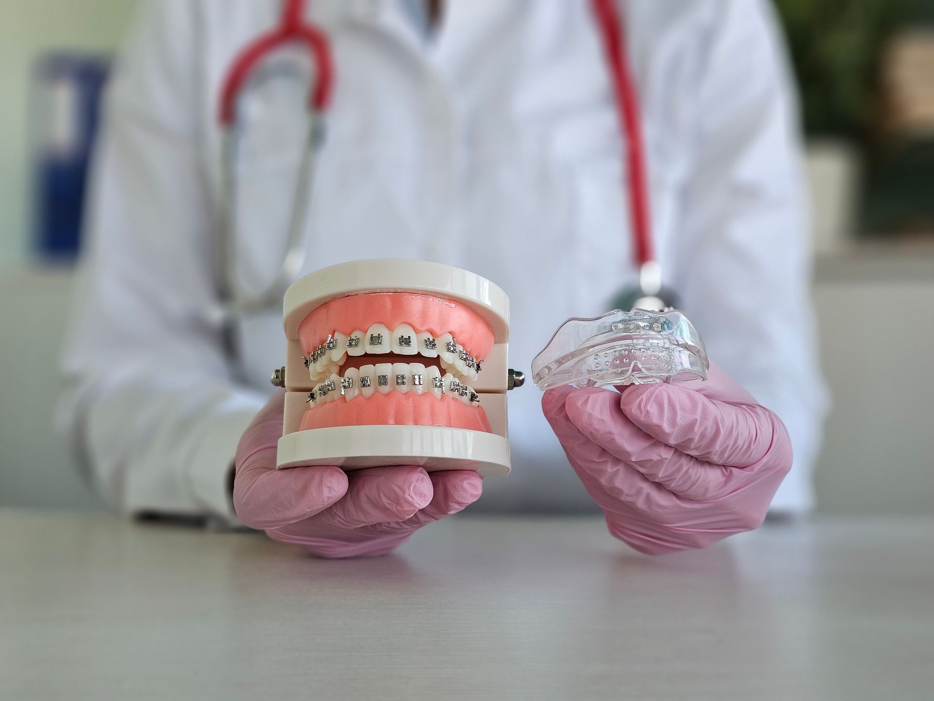 Person in gloves holding dental models, one with braces and one with an aligner.