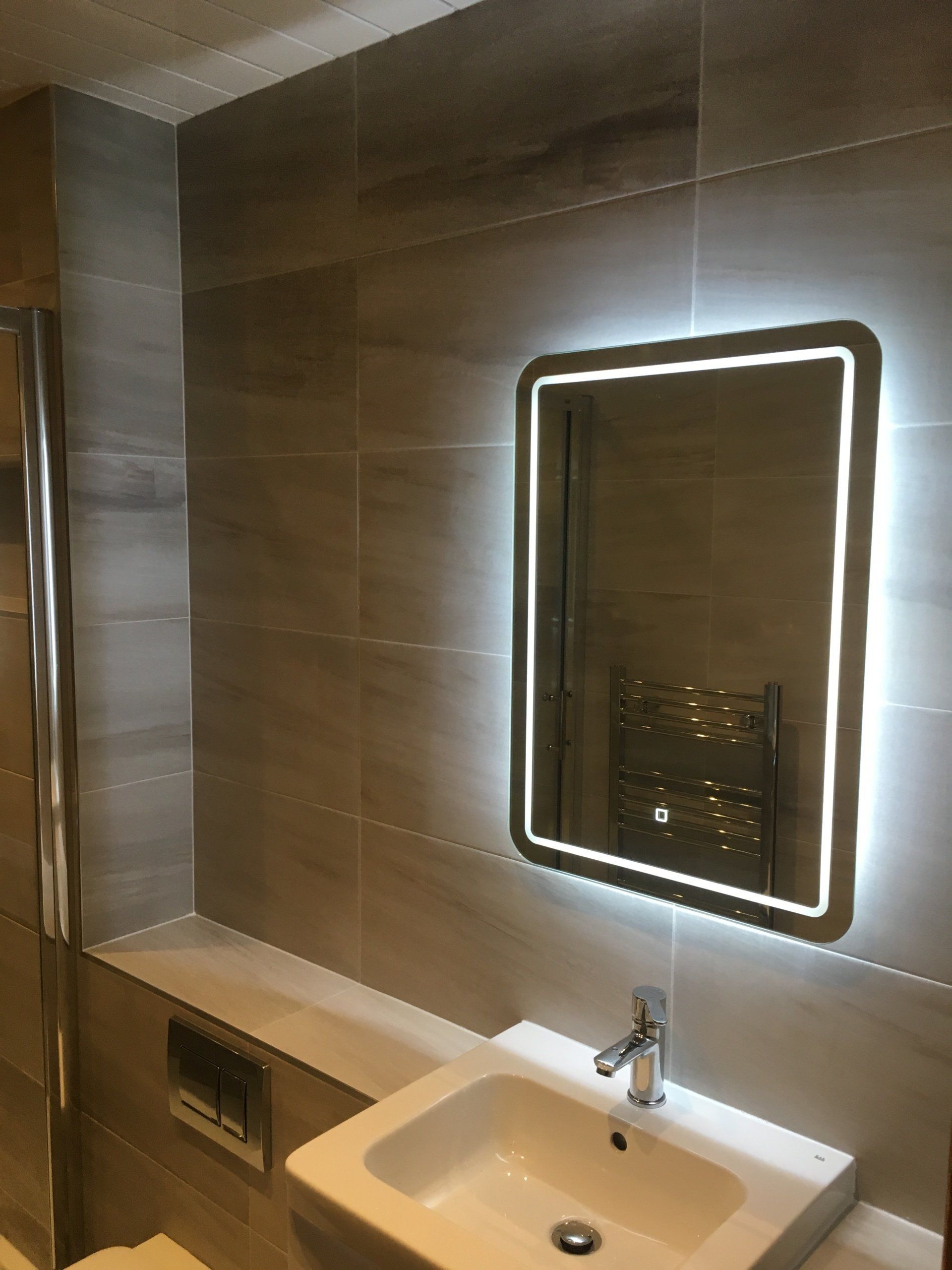 Ensuite bathroom grey tiles illuminated mirror and white wall hung vanity unit