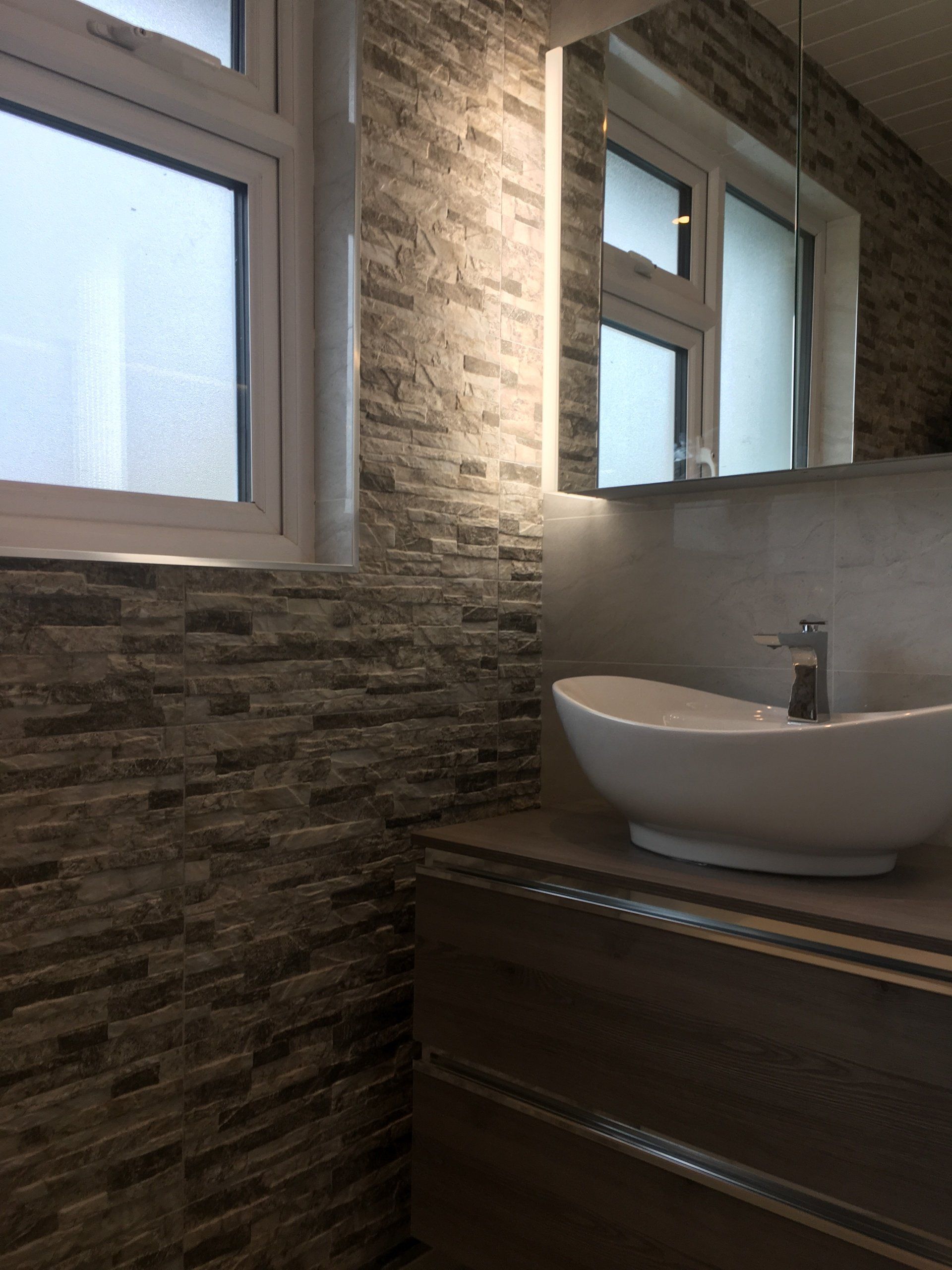 Bathroom stone effect tiles and dark wood wall hung vanity unit with countertop basin and illuminated mirror cabinet