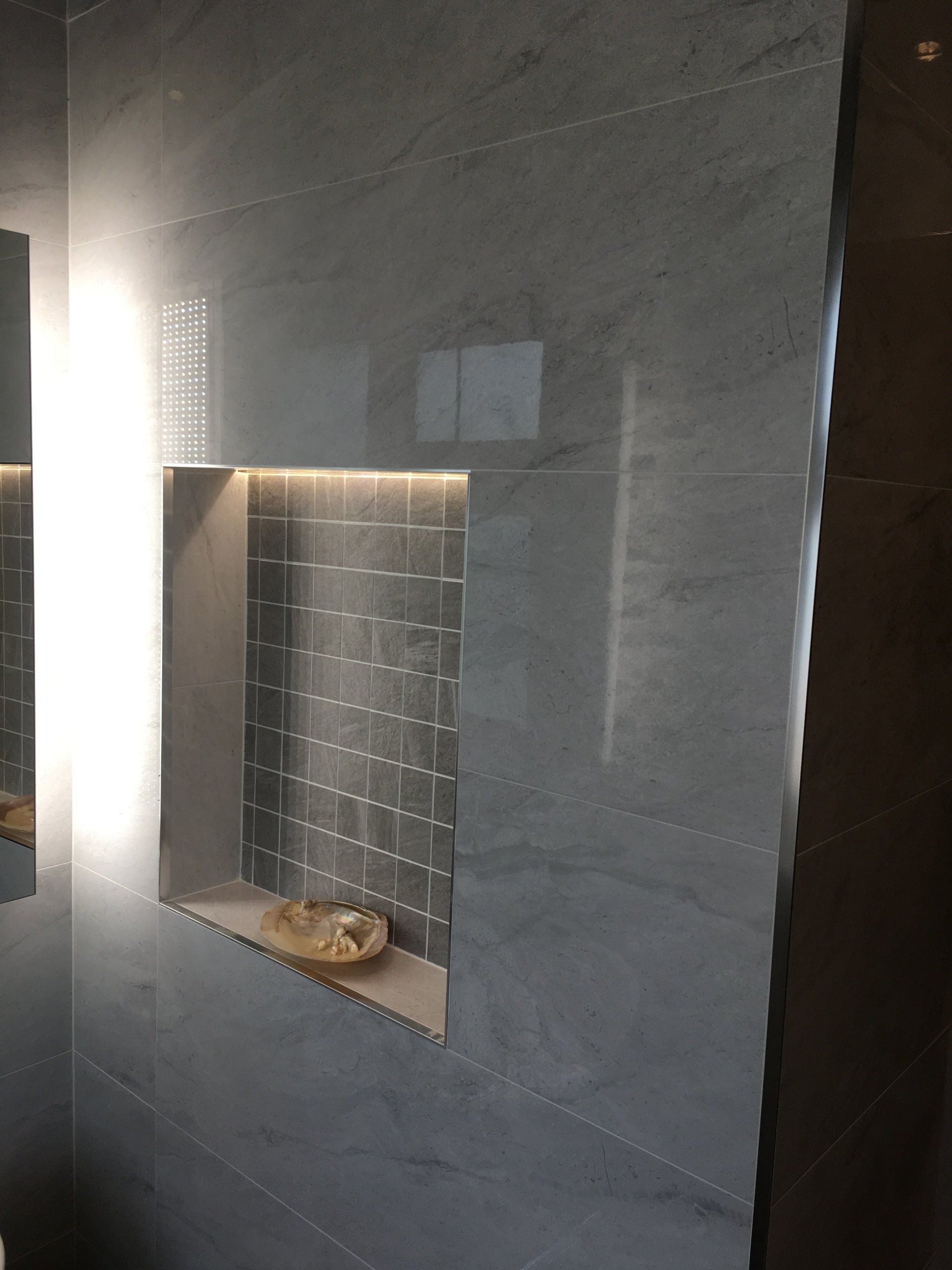 Bathroom with grey tiles and recessed illuminated shelf with decoration