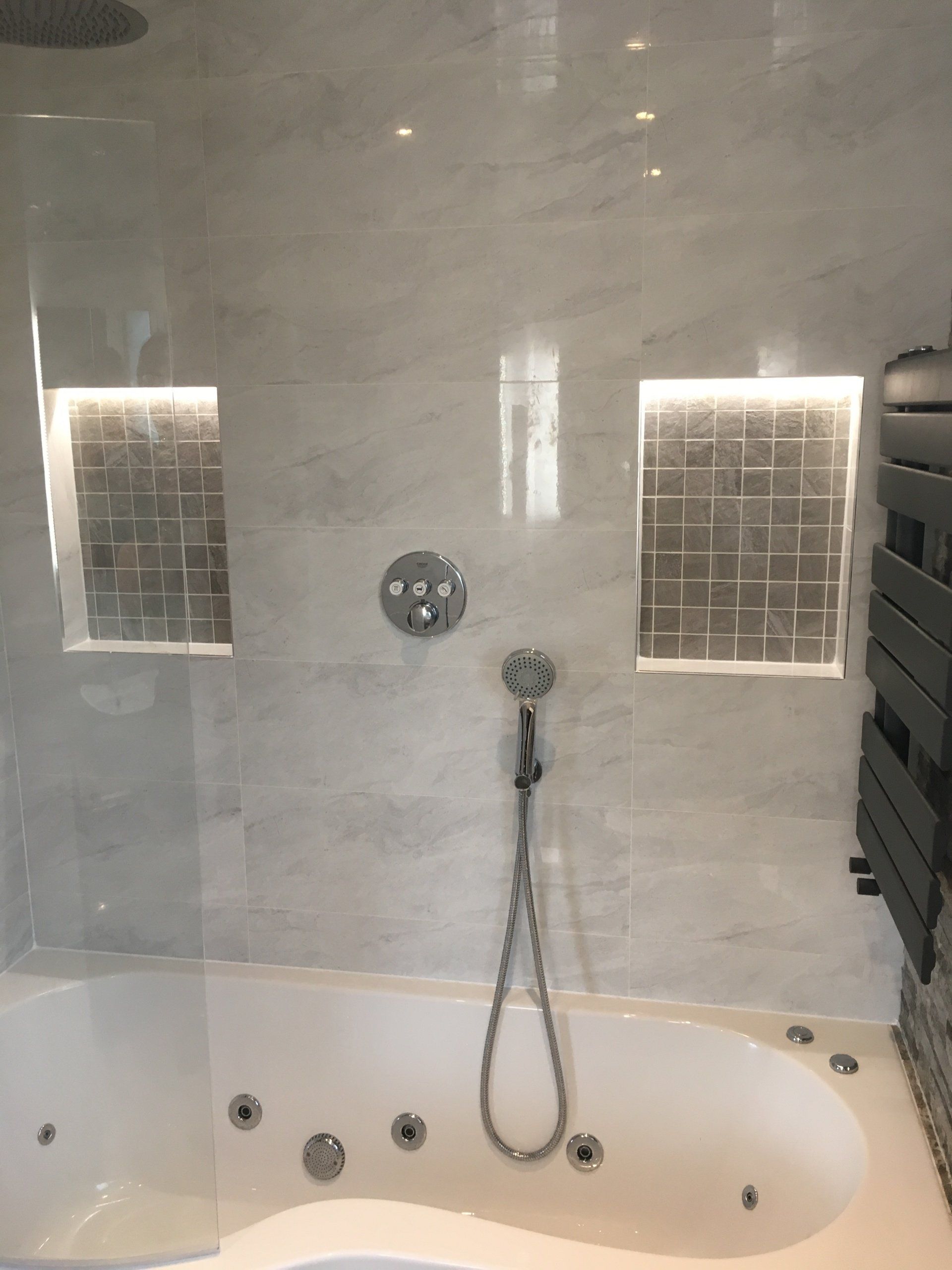 Bathroom with grey tiles jacuzzi bath and two recessed illuminated shelves