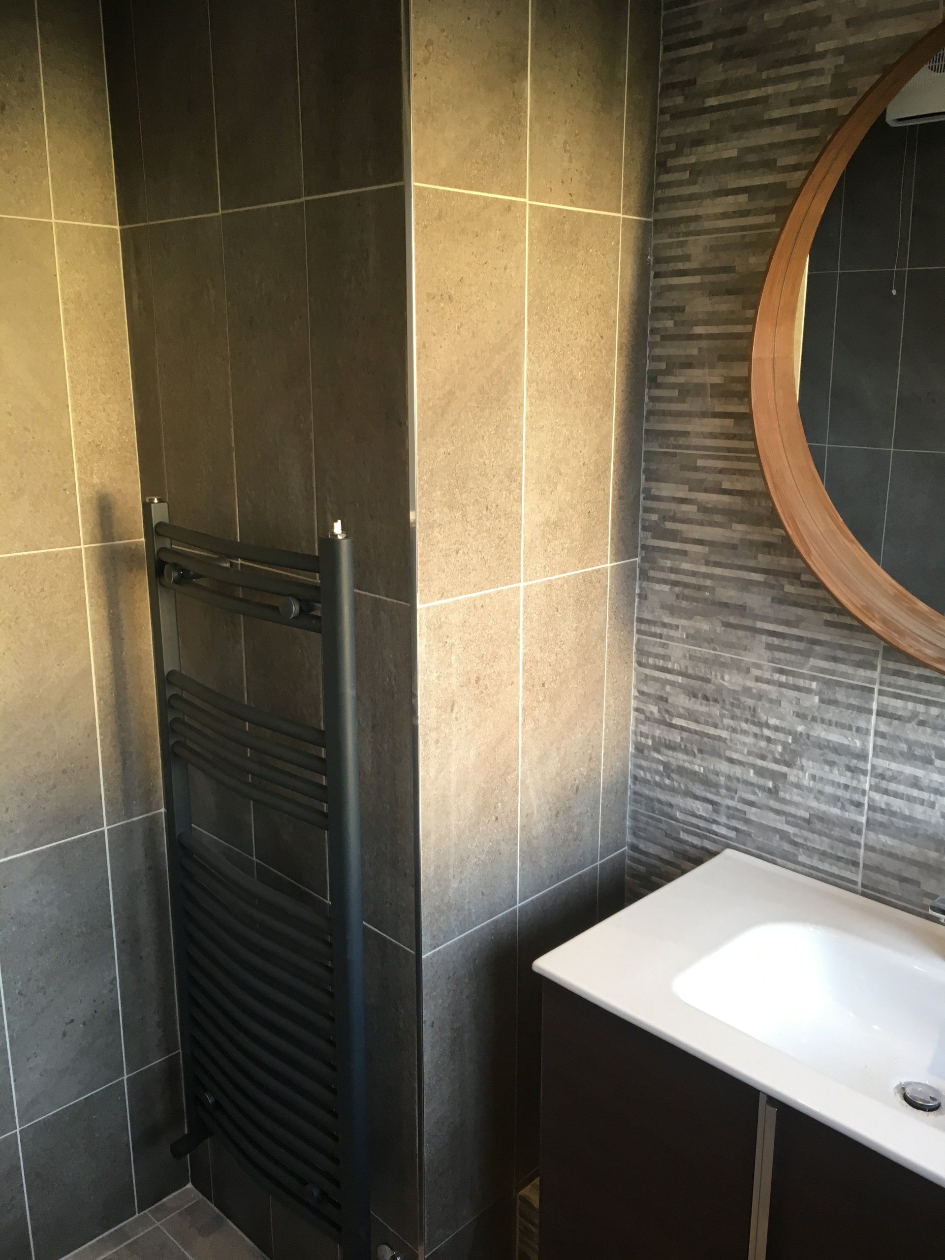 Bathroom dark tiles heated towel rail wall hung vanity unit and round mirror