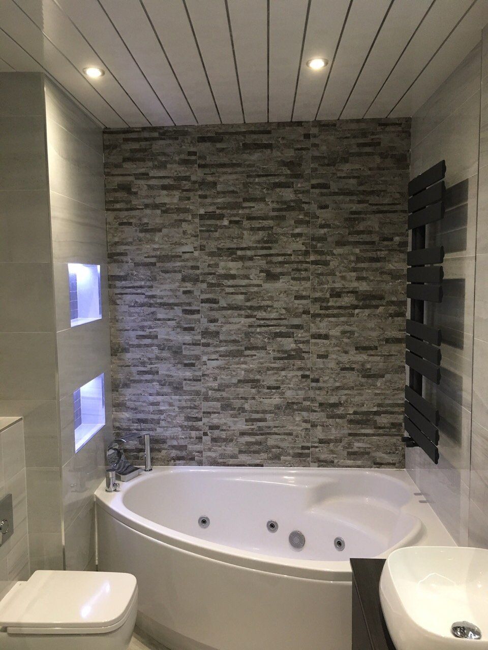 beautiful bathroom with Jacuzzi bath, stone effect tiles, anthracite heated towel rail