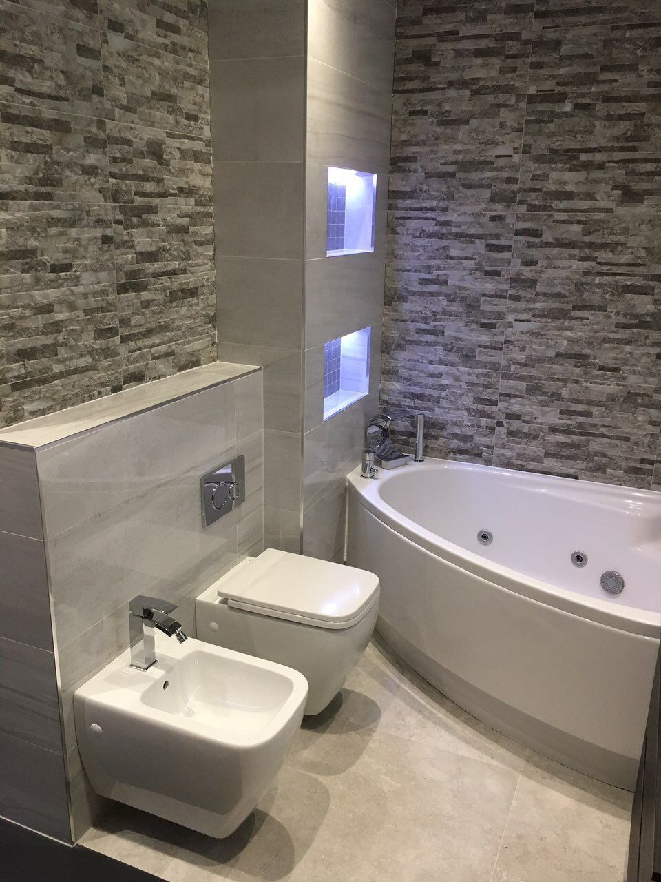 Bathroom with wall hung bidet and toilet, jacuzzi bath and stone effect tiles