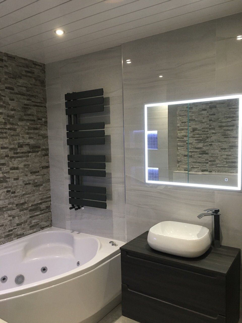 bathroom with jacuzzi bath, grey tiles and dark wall hung vanity unit with countertop basin