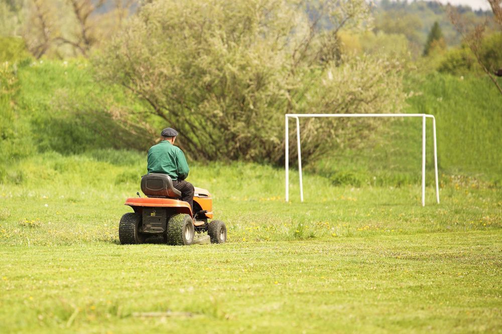 A Man is Riding a Lawn Mower in a Field Next to a Soccer Goal — Collis Care In Dundowran, QLD