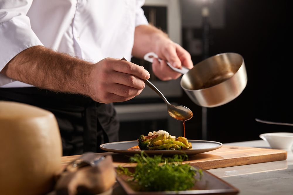 A Chef is Pouring Sauce on a Plate of Food With a Spoon — Collis Care In Dundowran, QLD