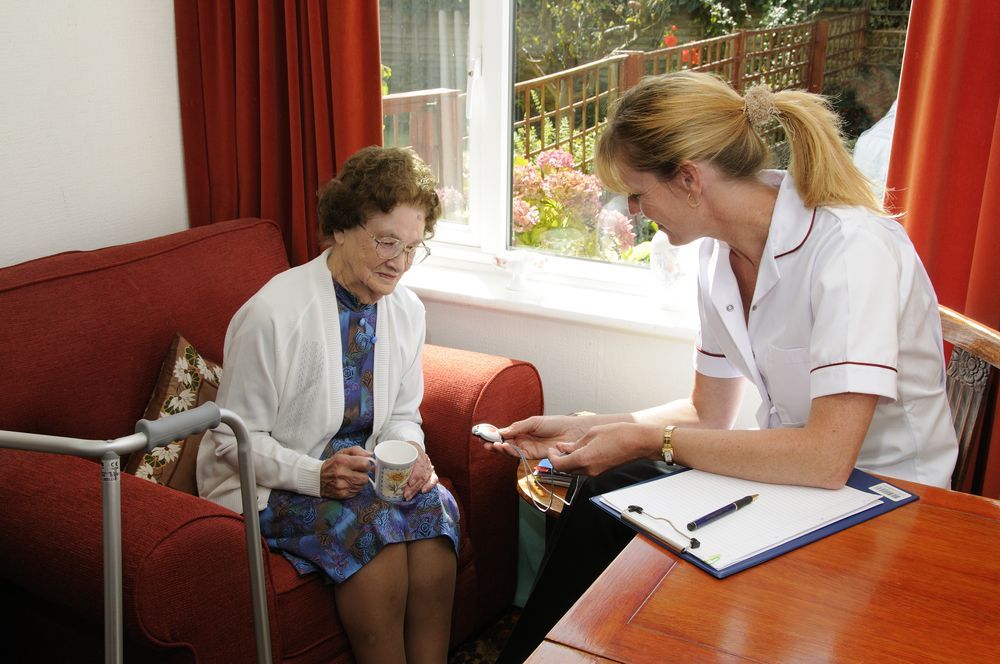 A Nurse is Talking to an Elderly Woman Who is Sitting on a Couch — Collis Care In Dundowran, QLD